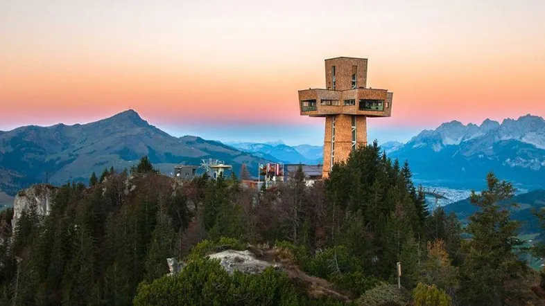 Ein markanter Aussichtsturm auf einem Berggipfel bei Sonnenuntergang mit weitem Blick über die Alpenlandschaft.