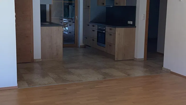 Heller offener Wohnbereich mit Holzboden und Blick auf die angrenzende Küche mit Fliesenboden.