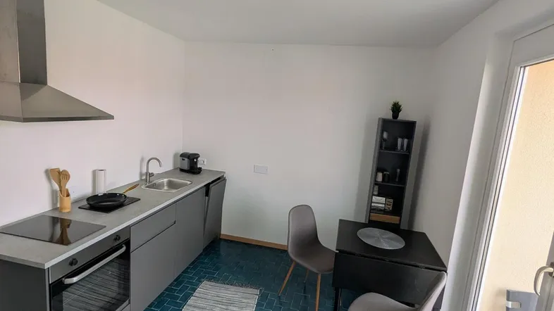 Moderne Küche mit blauen Fliesen, grauen Schränken, Induktionskochfeld und Zugang zum Balkon.