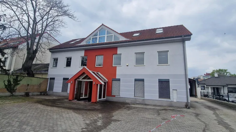 Modernes Gebäude mit auffälliger rot-grauer Fassade und vielen Fenstern, umgeben von einem gepflasterten Vorplatz.