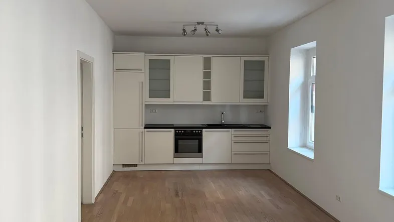 Heller Raum mit integrierter Küchenzeile, weißen Schränken und modernem Holzfußboden.