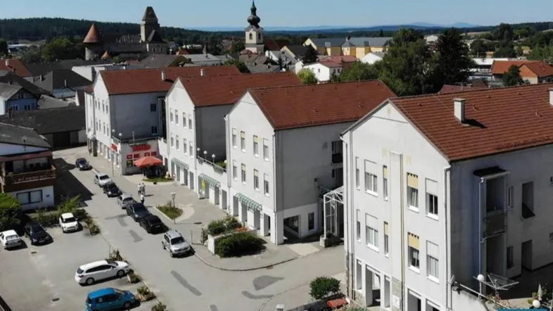 Luftaufnahme einer Kleinstadt mit Wohngebäuden, Straßen und Kirchtürmen im Hintergrund.