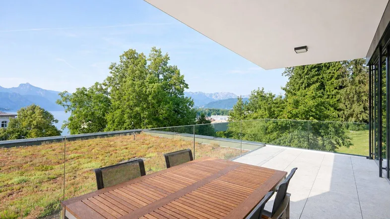 Geräumige Terrasse mit Esstisch, Glasgeländer und weitem Blick auf den See und die Berge.