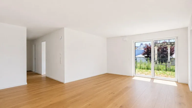 Heller, leerer Wohnraum mit Holzboden, großen Schiebetüren und Blick ins Grüne.