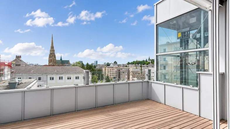 Großer Balkon mit Holzboden und weitem Blick über die Stadt und eine Kirche.