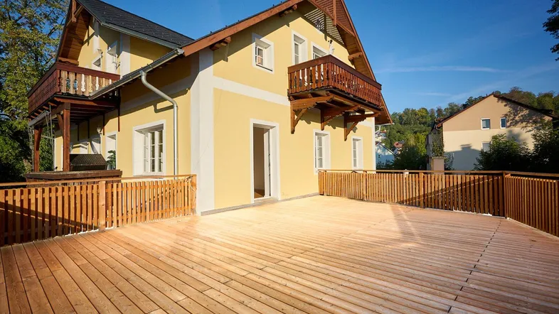 Große Holzterrasse vor einem charmanten Haus mit gelber Fassade und Holzbalkonen.