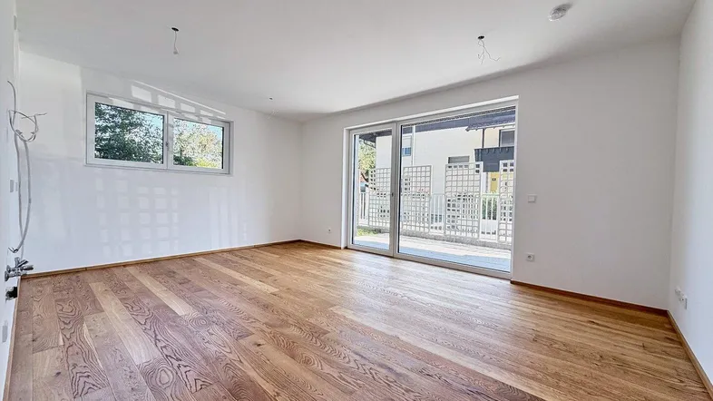 Heller, leerer Raum mit hochwertigem Holzboden und großem Schiebefenster zum Balkon.