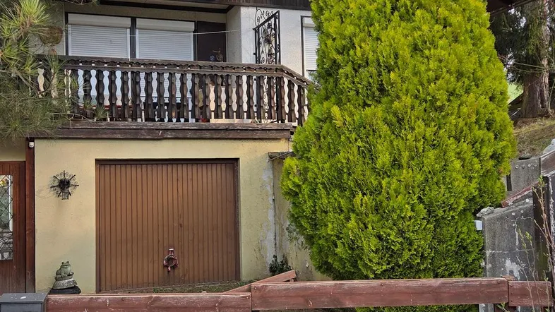 Vorderansicht eines Hauses mit Holzbalkon, Garage und umzäuntem Vorgartenbereich.
