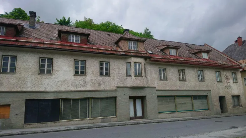 Altes Gebäude mit mehreren Fenstern und Ladenfronten an einer Straße unter bewölktem Himmel.
