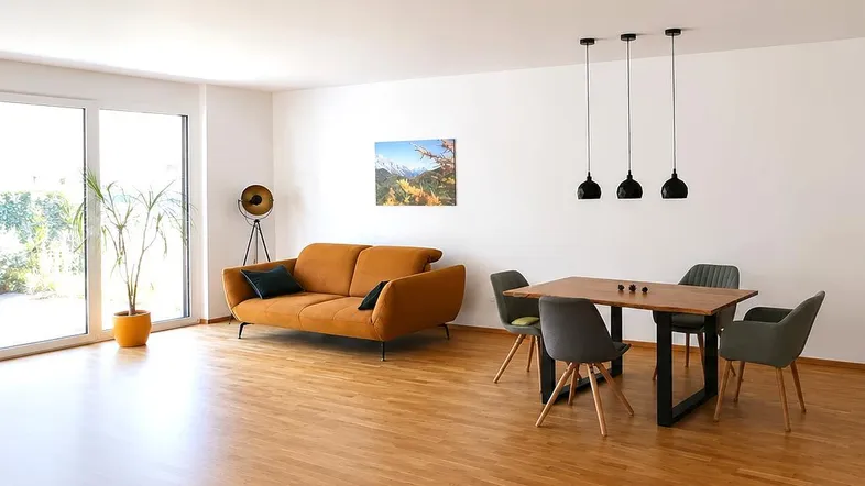 Heller offener Wohn- und Essbereich mit modernem Sofa, Holztisch und Zugang zum Garten.
