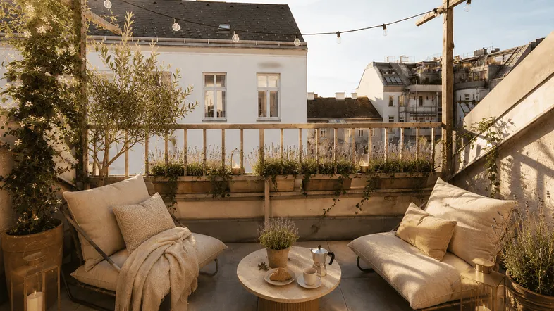 Gemütliche Dachterrasse mit bequemen Loungemöbeln, Pflanzen und stimmungsvoller Beleuchtung bei Sonnenuntergang.