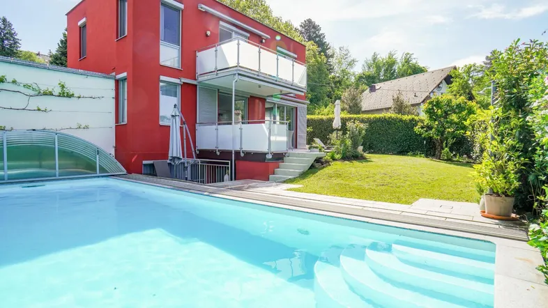 Modernes Haus mit roter Fassade, großem Pool und gepflegtem Gartenbereich.