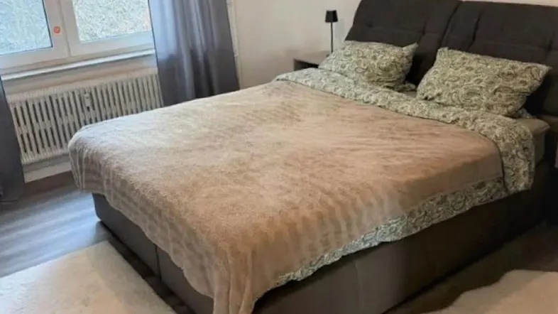 Gemütliches Schlafzimmer mit großem Bett, Laminatboden und Fenster mit Vorhängen.