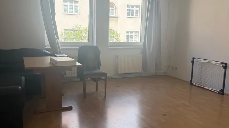 Helles Wohnzimmer mit Parkettboden, großen Fenstern und Blick auf die gegenüberliegenden Gebäude.