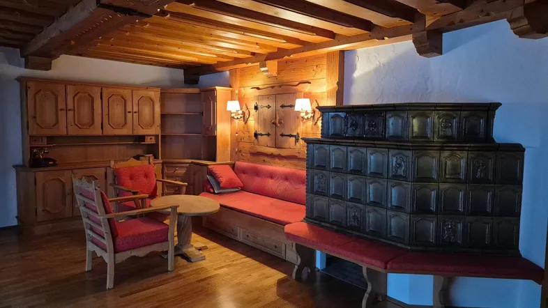 Gemütliches Wohnzimmer im alpinen Stil mit Holzbalkendecke, Kachelofen und traditionellen Möbeln.