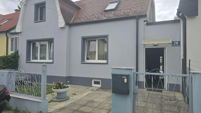 Graues Einfamilienhaus mit Mansarddach, weiß gestrichenen Fenstern und einem kleinen Vorgarten.