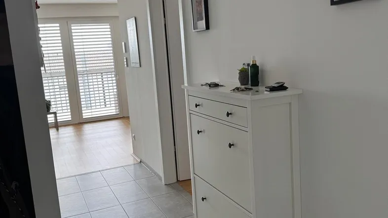 Heller Flur mit Fliesenboden, Schuhschrank und Zugang zu weiteren Räumen.