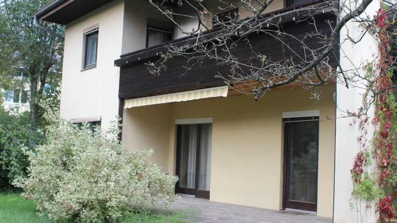 Ansicht des Hauses von der Gartenseite mit Rasenfläche, Terrasse und Balkon im Obergeschoss.