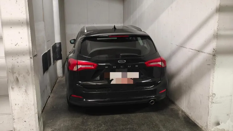 Schwarzes Auto in einer engen Tiefgaragenparklücke mit Betonwänden und Deckeninstallationen.