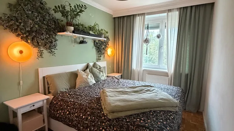 Gemütliches Schlafzimmer mit grüner Akzentwand, Pflanzen und klassischem Parkettboden.