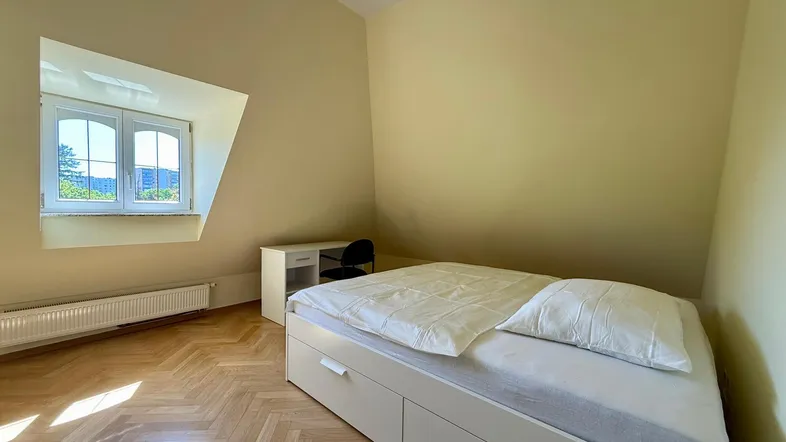 Helles Schlafzimmer im Dachgeschoss mit Dachschrägen, Parkettboden und einem Fenster mit Ausblick.