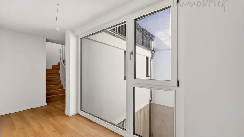 Heller Eingangsbereich mit Holzboden, großem Fenster und einer eleganten Holztreppe.