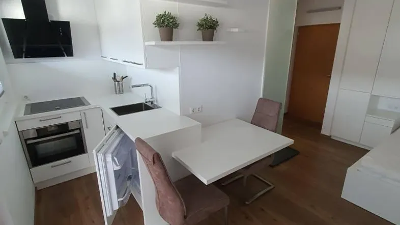 Moderne Küchenzeile mit integriertem Essbereich, weißen Schränken und Holzboden in einem Studioapartment.