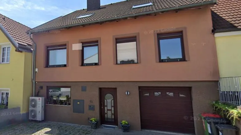 Fassade eines Einfamilienhauses mit braunem Putz, Fenstern und Garagentor.