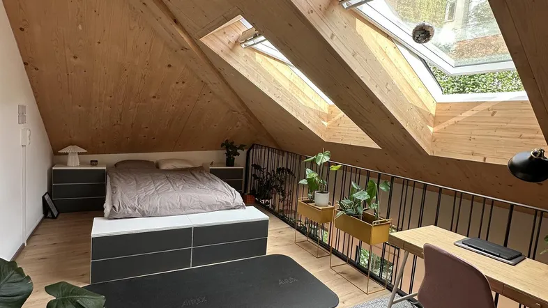 Helles Schlafzimmer im Dachgeschoss mit Holzverkleidung, Dachfenstern und integriertem Arbeitsbereich.