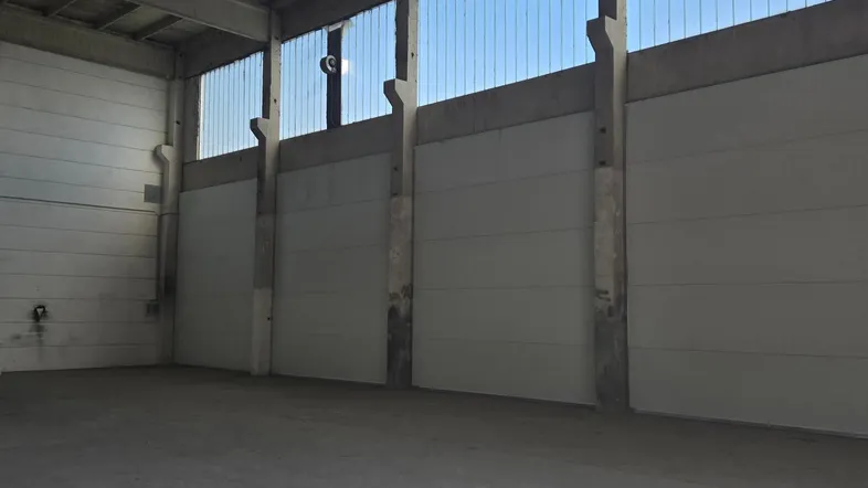 Geräumige Industriehalle mit Betonboden, hohen Decken und viel Tageslicht durch die oberen Fensterbereiche.