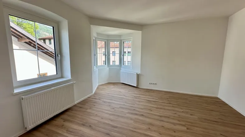 Geräumiges Wohnzimmer mit hellem Laminatboden und einem charmanten Erkerfenster, das viel Licht spendet.