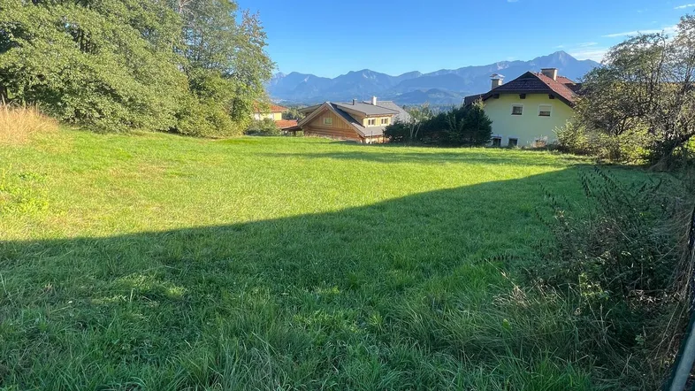 Grünes Grundstück mit Blick auf die umliegende Landschaft und Berge unter blauem Himmel.