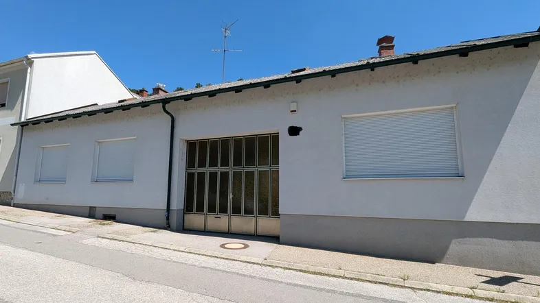 Fassade eines Gebäudes mit Garagentor und Rollläden unter blauem Himmel.