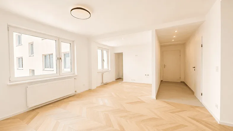 Helles, offenes Wohnzimmer mit Fischgrätparkett und großen Fenstern, die viel Tageslicht hereinlassen.