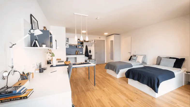 Helles Studio-Apartment mit zwei Betten, Schreibtischbereich und integrierter Küchenzeile.
