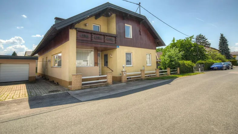 Ansicht des Hauses von der Straße mit Garage und Vorgarten bei sonnigem Wetter.