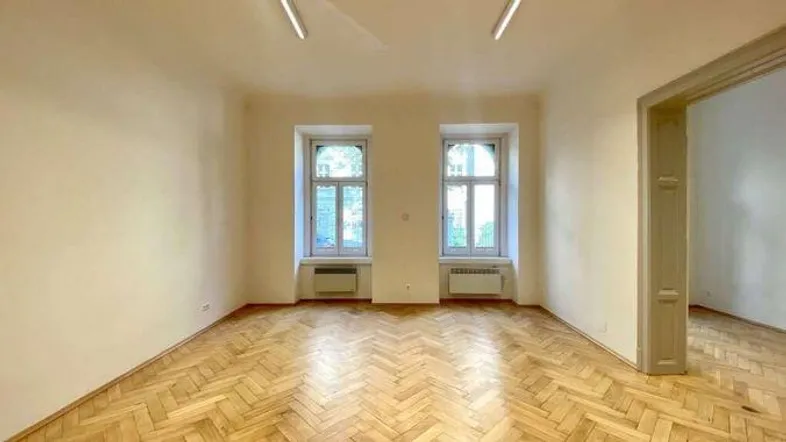 Heller Wohnraum mit Fischgrätparkettboden, hohen Decken und zwei großen Fenstern mit Grünblick.