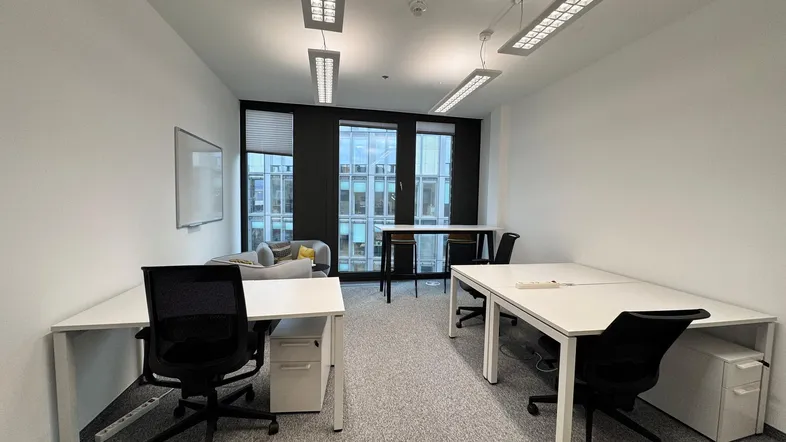 Modernes Büro mit mehreren Arbeitsplätzen, großen Fenstern und Teppichboden für eine produktive Arbeitsumgebung.