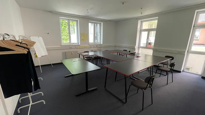 Geräumiger Konferenzraum mit U-förmiger Tischordnung, Teppichboden und großen Fenstern mit Grünblick.