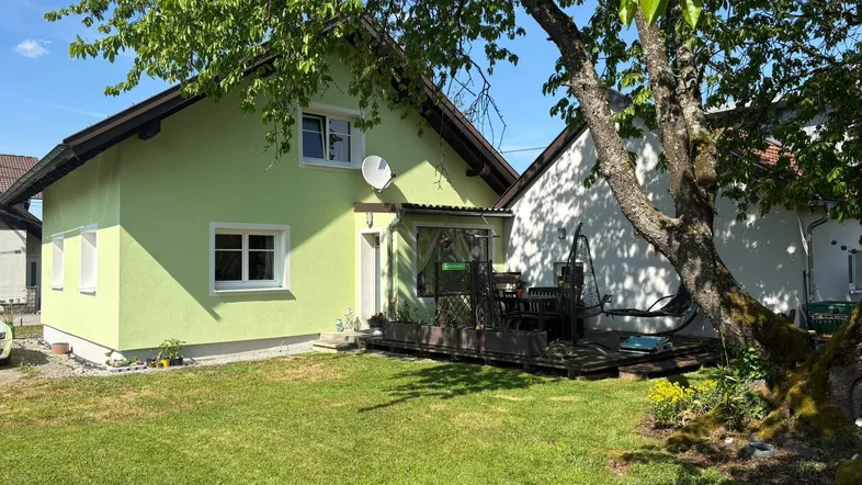 Grünes Einfamilienhaus mit gepflegtem Rasen und altem Baum im Vorgarten an einem sonnigen Tag.