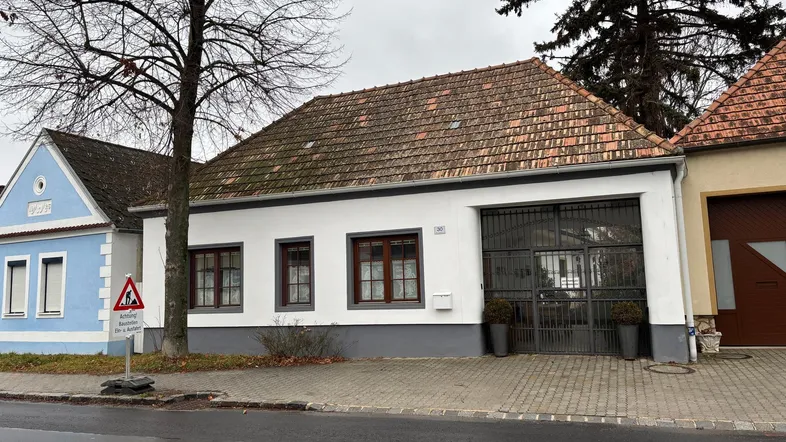 Weißes Haus mit braunem Ziegeldach und großen Fenstern an einer Straße gelegen.