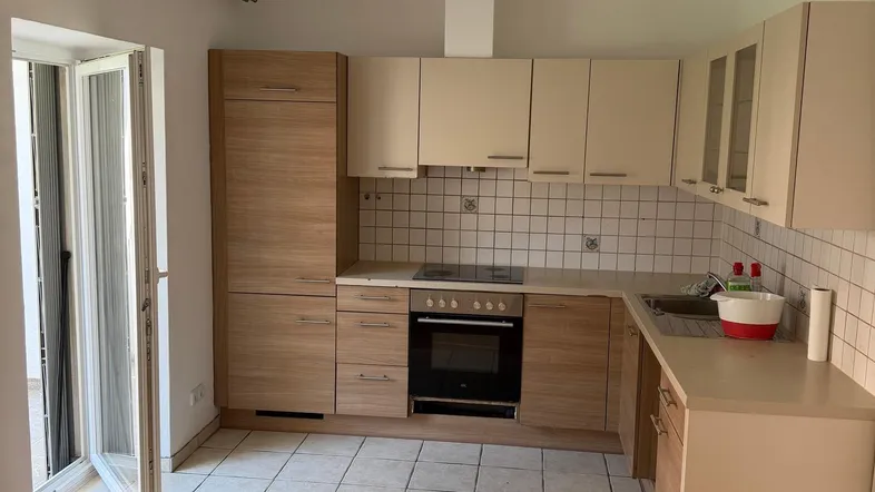 Helle Küche mit Holz- und Beigefarbenen Schränken, Fliesenboden und Zugang zu einem Außenbereich.