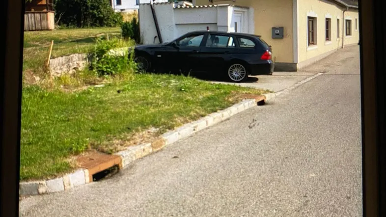 Gelbes Einfamilienhaus mit schwarzem Auto davor und Grünfläche im Vordergrund.