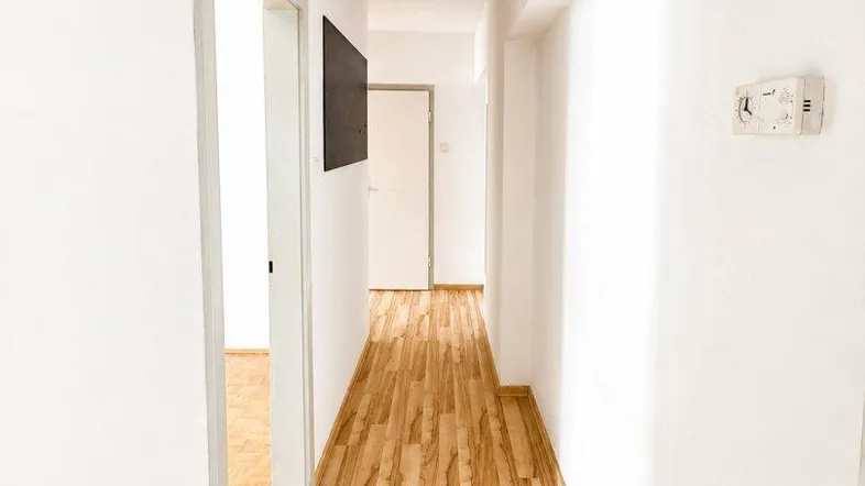Heller Flur mit modernem Laminatboden und weißen Wänden, der zu weiteren Räumen führt.