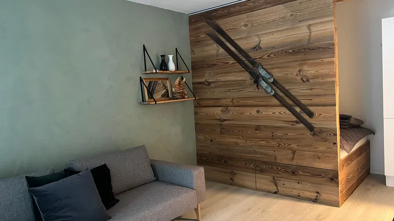 Gemütliches Wohnzimmer mit moderner Couch, Holzvertäfelung und alpiner Dekoration.