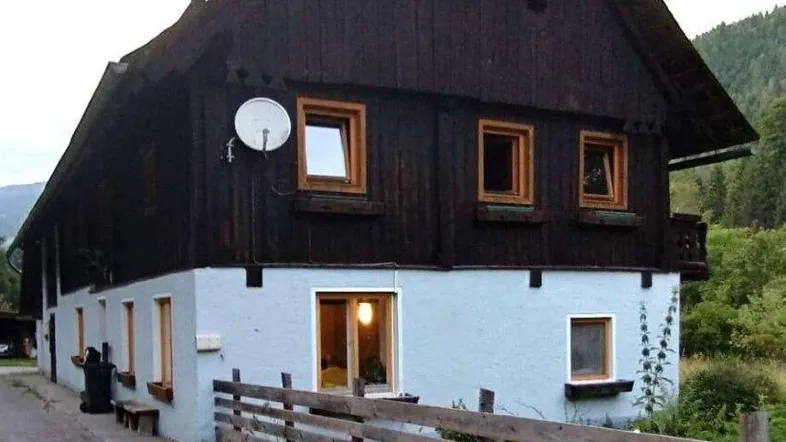 Traditionelles Haus mit dunkler Holzfassade und hellem Sockel in ländlicher Umgebung.