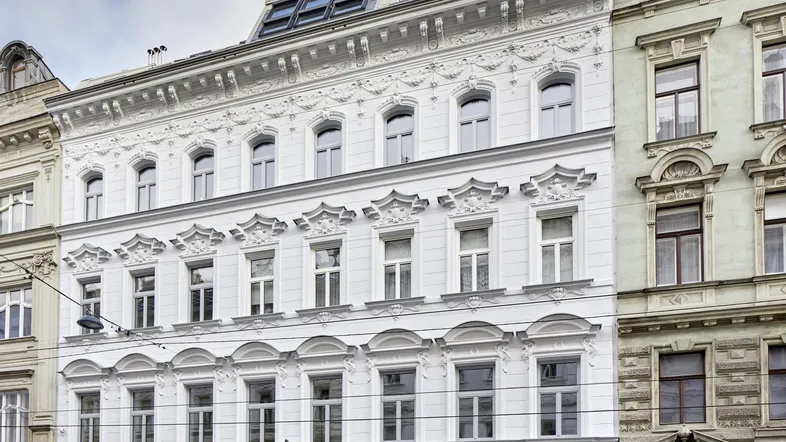 Elegante weiße Fassade eines historischen Gebäudes mit aufgesetztem modernen Dachgeschoss.