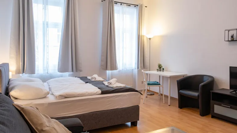 Helles Zimmer mit Doppelbett, Sofa und kleinem Esstisch, ideal für ein Studio-Apartment.