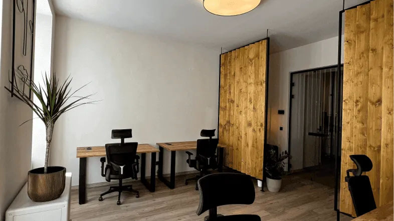 Modernes Büro mit mehreren Arbeitsplätzen, Holztrennwänden und hellem Boden, gut beleuchtet durch Tageslicht.