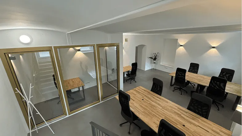 Geräumiger Büroraum mit modernen Holzschreibtischen, ergonomischen Stühlen und Glasabtrennungen für Besprechungsbereiche.